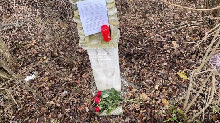 Blumen vor der zerstörten Skulptur "Grenzen Küssen", einem Denkmal der Liebe